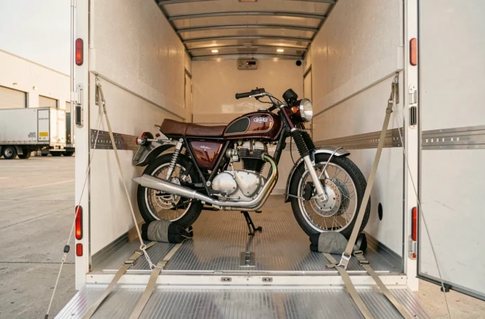 Moto vintage bordeaux et chromée arrimée à l'intérieur d'un camion de transport fermé avec des sangles et des cales de roue
